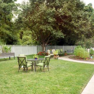 A tranquil backyard garden with outdoor seating, surrounded by greenery and a white fence.