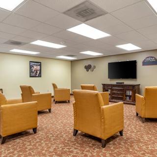 A cozy lounge area with several yellow armchairs facing a television on the wall.