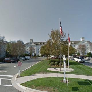 A large building with multiple floors is surrounded by a parking lot, featuring flags and trees in the foreground.