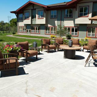 An inviting outdoor patio area with comfortable seating and a fire pit in front of a modern building.