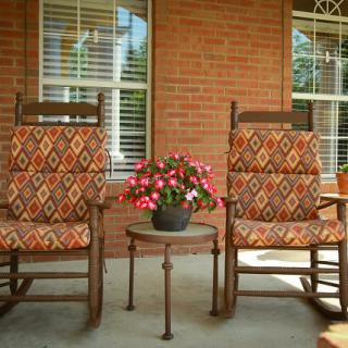 Two patterned rocking chairs on a porch with a flower pot between them.