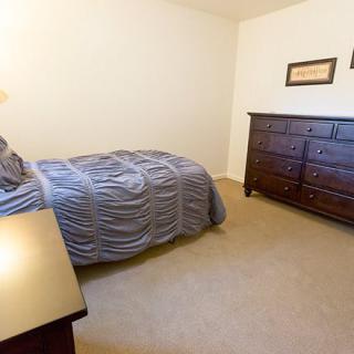 A cozy bedroom featuring a single bed, dresser, and lamp.