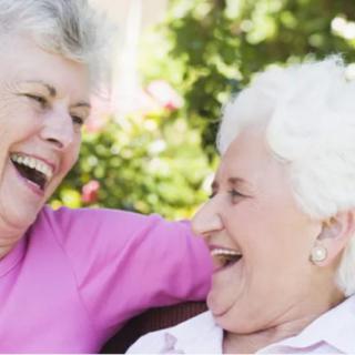 Two elderly women laughing together outdoors.