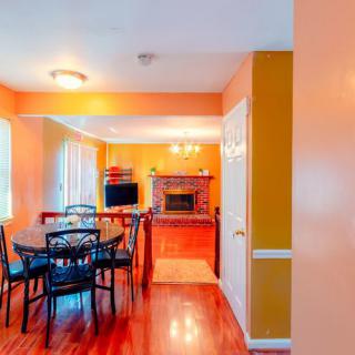 A cozy dining area with warm orange walls and hardwood floors, featuring a table set for six, a fireplace, and a television.