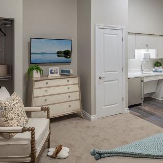 A cozy bedroom with modern furnishings, featuring a dresser with a television on top and an armchair beside it.