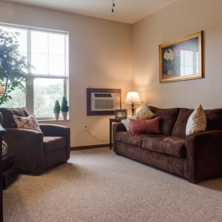 A cozy living room with a brown sofa, armchair, and a window providing natural light.