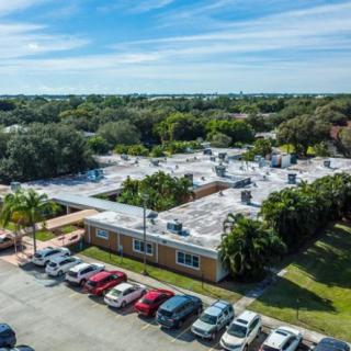 Aerial view of a building with a parking lot surrounded by trees on a sunny day.