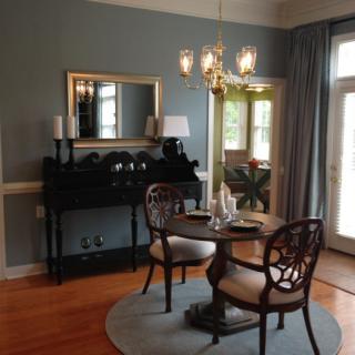 A cozy dining area with elegant furniture and a chandelier, complemented by natural light from large windows.