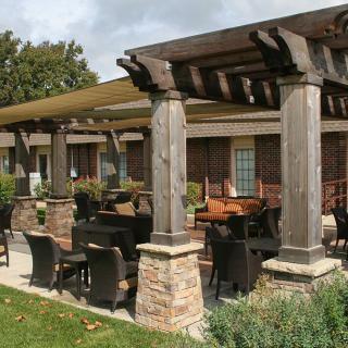 An outdoor patio with a pergola and comfortable seating, surrounded by greenery.