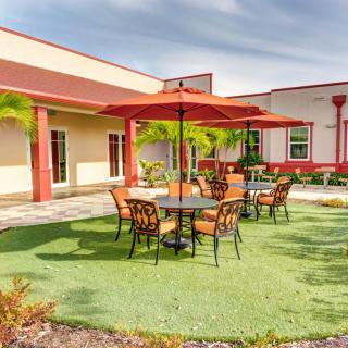 A sunny patio area with tables, chairs, and umbrellas outside a building.