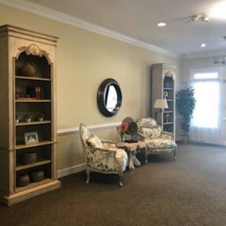 A cozy living room with elegant furniture, featuring two cushioned chairs, ornamental shelves, and a round mirror.