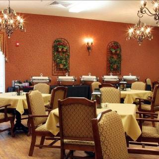 An elegant dining room with chandeliers, decorated walls, and neatly arranged tables and chairs.