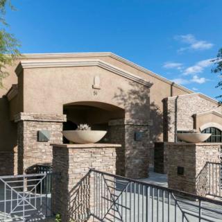 A modern residential building with a stone facade and architectural details, set against a clear blue sky.