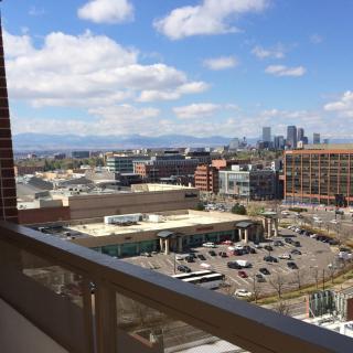 A cityscape view from a balcony overlooking downtown with buildings and a partly cloudy sky.