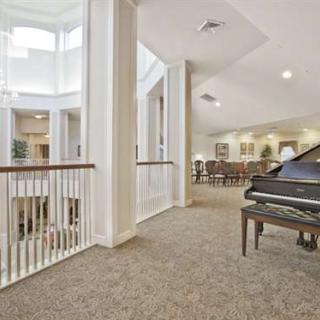 A bright and spacious interior with a grand piano, carpeted floors, and an elegant railing.
