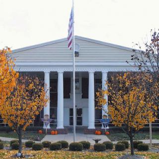 A classic government building featuring columns, surrounded by trees in autumn colors with a flag waving in front.