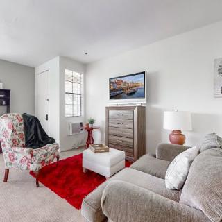 A cozy living room with a sofa, floral armchair, and a red rug, featuring a wall-mounted television and stylish decor.