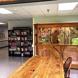 A cozy library corner featuring bookshelves and a large wooden table with a view outside.