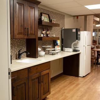 A cozy kitchen area featuring wooden cabinets, a refrigerator, microwave, and open shelves on a wood floor.
