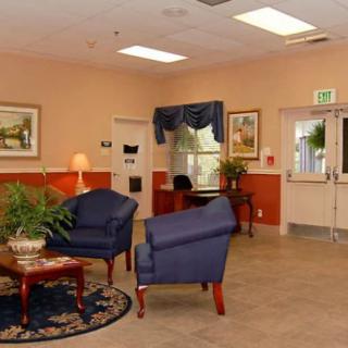 A cozy lobby area with blue chairs, a wooden table, and plants, creating a welcoming atmosphere.