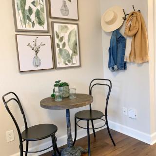 A cozy corner with a small table and chairs, adorned with botanical wall art and hanging hats and jackets.