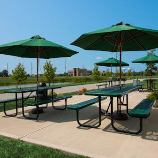 A sunny outdoor picnic area featuring green tables and umbrellas, ideal for relaxation and gatherings.