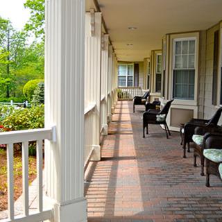A long porch with outdoor seating and columns, featuring a brick floor.