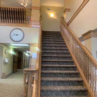 A view of a staircase with wooden railing leading to an upper floor, featuring a clock on the wall.