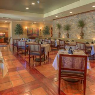 Elegant restaurant interior with neatly arranged tables and chairs, featuring a decorative brick wall and potted plants.