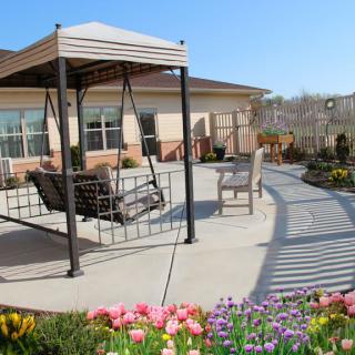 A cozy patio area with a swing under a pergola, surrounded by colorful flowers.