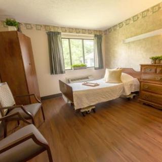A well-lit hospital patient room featuring a bed, a window with curtains, and wooden furniture.