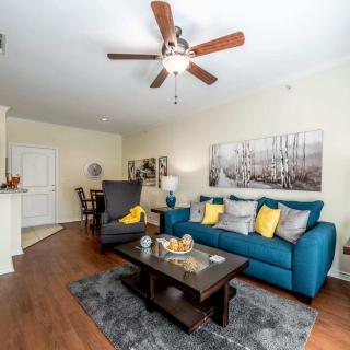 A modern living room with a teal sofa and yellow pillows, featuring a coffee table and ceiling fan.