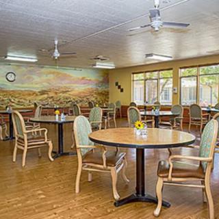 A spacious dining area featuring round tables and chairs, with a scenic mural on one wall and large windows allowing natural light.