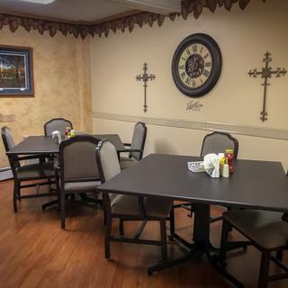A cozy dining area with tables and chairs, featuring wall decor including a large clock and crosses.