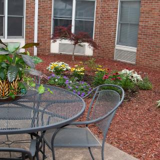 A cozy patio garden with outdoor furniture and vibrant flowers against a brick building backdrop.