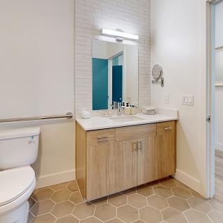 A modern bathroom with a wooden vanity, sink, mirror, and toilet.