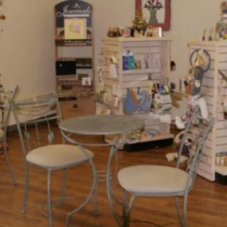 A cozy store interior featuring a small table and chairs surrounded by shelves of gifts and decor items.