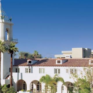 A historic building featuring Spanish-style architecture, complemented by palm trees and a clear blue sky.