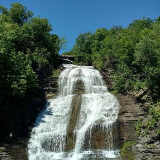 A beautiful waterfall cascading down a rocky cliff surrounded by lush green trees under a clear blue sky.
