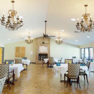 A spacious dining area with elegant chandeliers, neatly arranged tables, and patterned chairs.