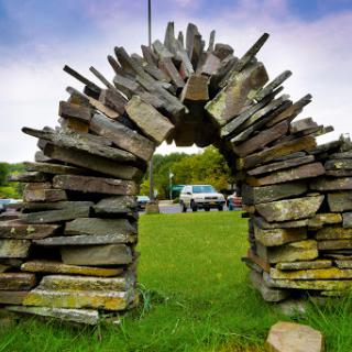 A beautifully crafted stone archway made from layered stones, set against a lush green backdrop.