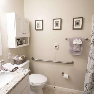 A neatly organized bathroom with modern amenities including a toilet, sink, and grab bar, complemented by wall art and a patterned shower curtain.