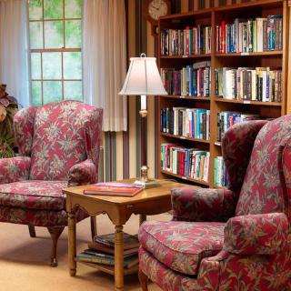 A cozy living room with patterned armchairs and a bookshelf.