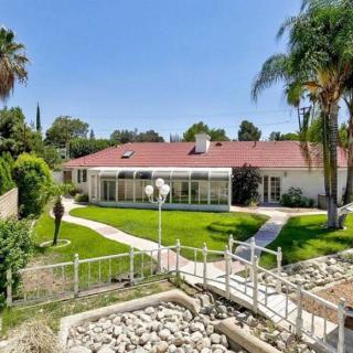 A view of a house with a spacious backyard featuring a green lawn, pathway, and palm trees.