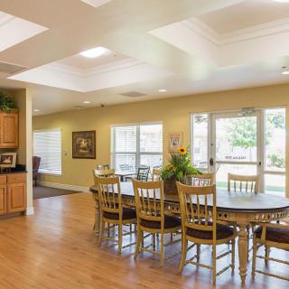 A bright dining area with a large table and wooden chairs, surrounded by windows.