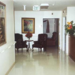 A hallway interior featuring a pair of chairs with a small table, a painting on the wall, and an exit sign above.