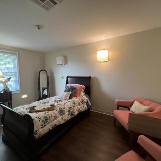A cozy, modern bedroom with a single bed, armchair, and natural lighting.