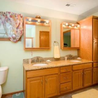 A bathroom featuring double sinks, wooden cabinets, and decorative mirrors with overhead lighting.