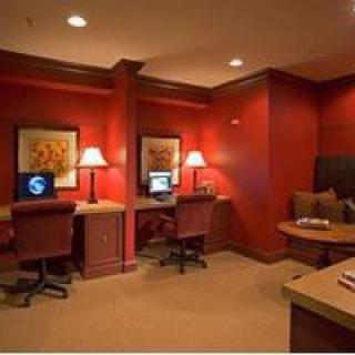 A cozy office space with two computer workstations, red walls, and warm lighting.