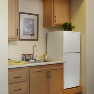 A compact kitchen space with a refrigerator, sink, and wooden cabinets.